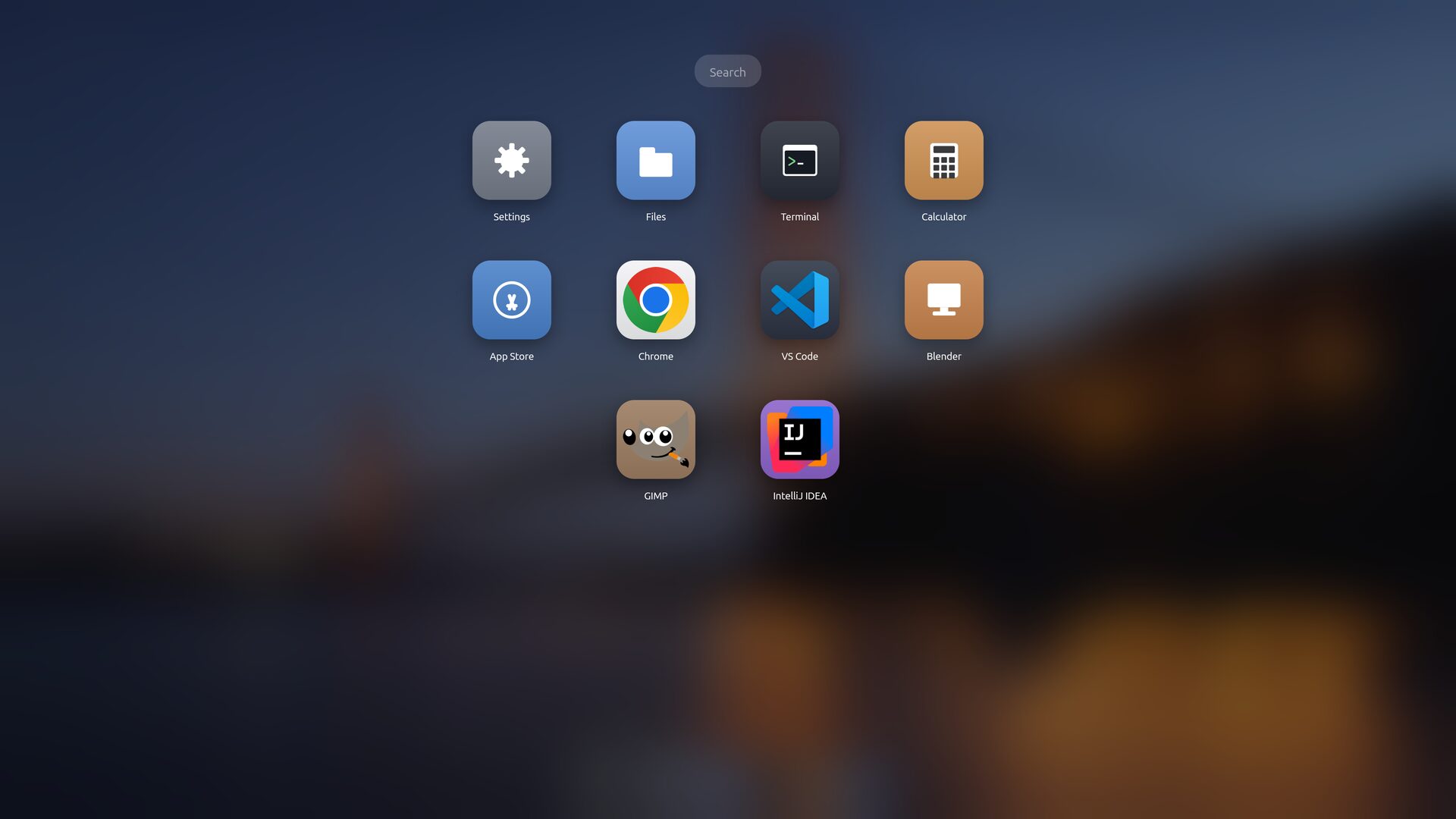 The Launchpad: a search box at the top and a grid of app icons — Settings, Files, Terminal, Calculator, App Store, Chrome, VS Code, Blender, GIMP and IntelliJ IDEA — over a blurred wallpaper.